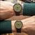 Herrenuhr am Handgelenk mit grünem Zifferblatt, orange Zeigern und braunem Lederarmband