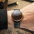 Sternglas Herrenuhr am Handgelenk, schwarzes Lederband und dunkelbraunes Zifferblatt mit goldenen Zeigern