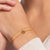 Goldfarbenes Armband am Handgelenk mit weißen Steinen und kleinem Anhänger
