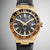 Armbanduhr front: schwarzes Zifferblatt mit goldenem Lünette-Design, schwarzes Lederband.