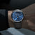 Herrenuhr am Handgelenk: blaues Zifferblatt, schwarzes Lederarmband, silbernes Gehäuse.