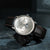 Sternglas Herrenuhr: dunkelbraunes Lederarmband und silberfarbenes Zifferblatt.