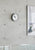 Kompakte Wanduhr mit weißem Zifferblatt, schwarzen Zeigern und roten Akzenten, an Betonwand