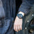 Herrenuhr am Handgelenk mit schwarzem Armband und blau-rotem Zifferblatt