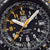 Detailansicht Herrenuhr: Zeiger und Leuchtzahlen auf schwarzem Zifferblatt.