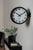 Wanduhr an der Wand mit schwarzem Rand, weißem Zifferblatt und rotem Sekundenzeiger