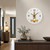 Wanduhr an der Wand mit weißem Zifferblatt, schwarzen Zeigern und goldenem Uhrwerk