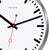 Detail der Wanduhr: weißes Zifferblatt, schwarze Zeiger, rote Sekundenanzeige, silberner Rand