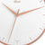 Nahaufnahme Wanduhr: roséfarbener Metallring, weißes Zifferblatt und schmale Zeiger